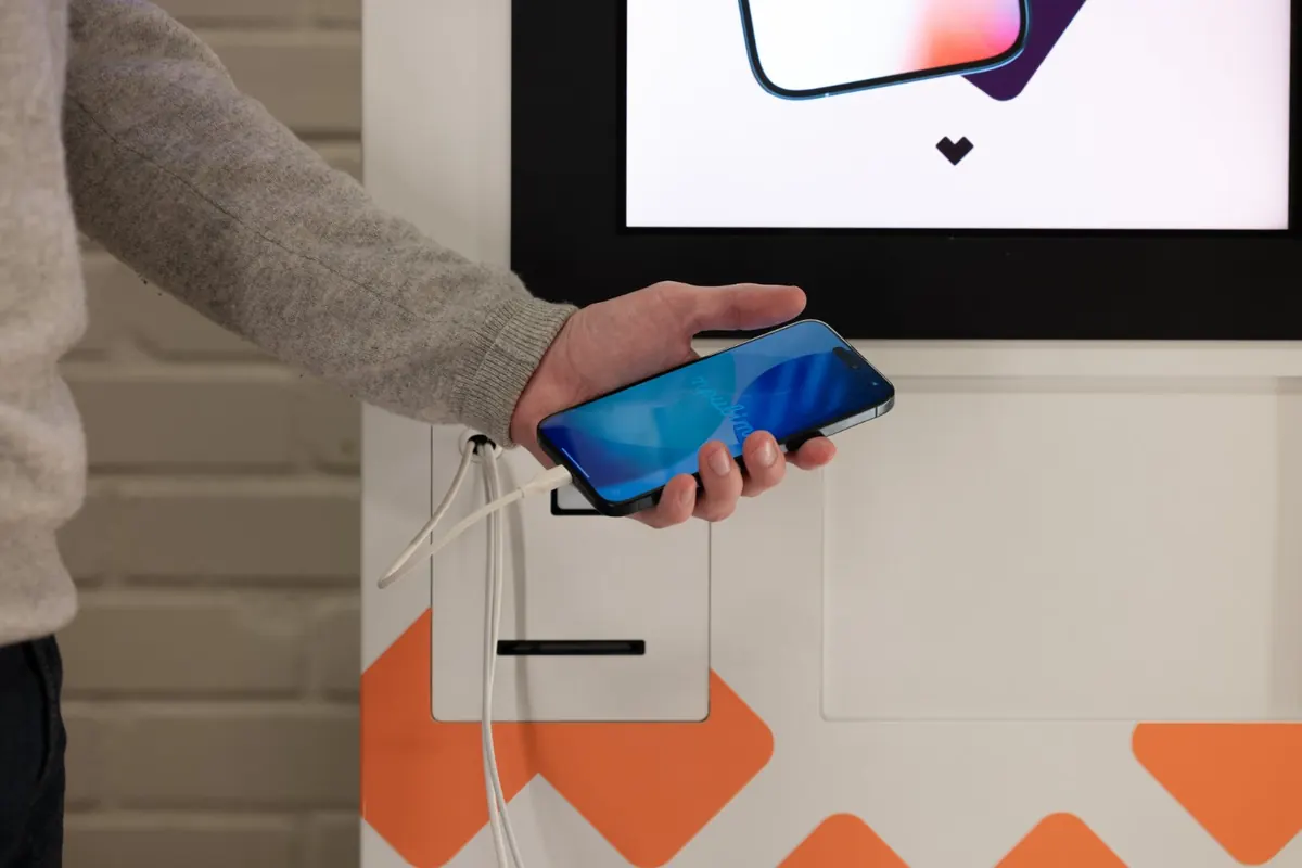 Hand som ansluter en iPhone till en Vendy-kiosk